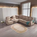 A detailed view of the Atlas Recliner Köşe Takımı, a contemporary L-shaped corner sectional sofa upholstered in textured beige fabric. The image shows its modern design with sleek lines and wide seats. The central console unit is featured, with an open lid, integrated cup holders, and a built-in Bluetooth speaker system visible on the side. The sofa is placed in a premium living room with light wood floors and textured wall paneling with LED backlighting.
