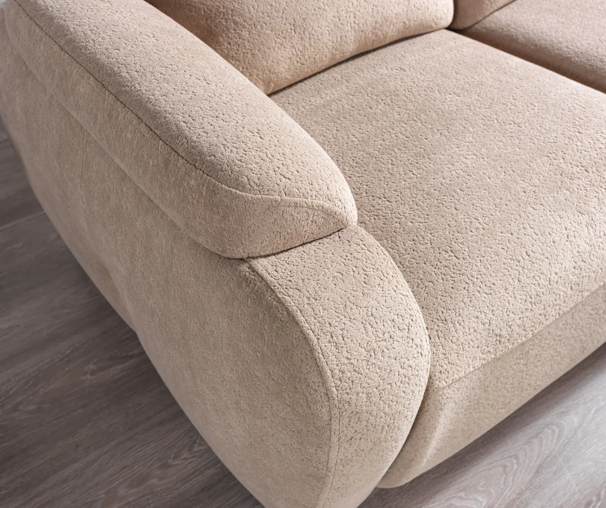 A detailed view of the Atlas Recliner Köşe Takımı, a contemporary L-shaped corner sectional sofa upholstered in textured beige fabric. The image shows its modern design with sleek lines and wide seats. The central console unit is featured, with an open lid, integrated cup holders, and a built-in Bluetooth speaker system visible on the side. The sofa is placed in a premium living room with light wood floors and textured wall paneling with LED backlighting.