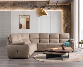 A detailed view of the Atlas Recliner Köşe Takımı, a contemporary L-shaped corner sectional sofa upholstered in textured beige fabric. The image shows its modern design with sleek lines and wide seats. The central console unit is featured, with an open lid, integrated cup holders, and a built-in Bluetooth speaker system visible on the side. The sofa is placed in a premium living room with light wood floors and textured wall paneling with LED backlighting.