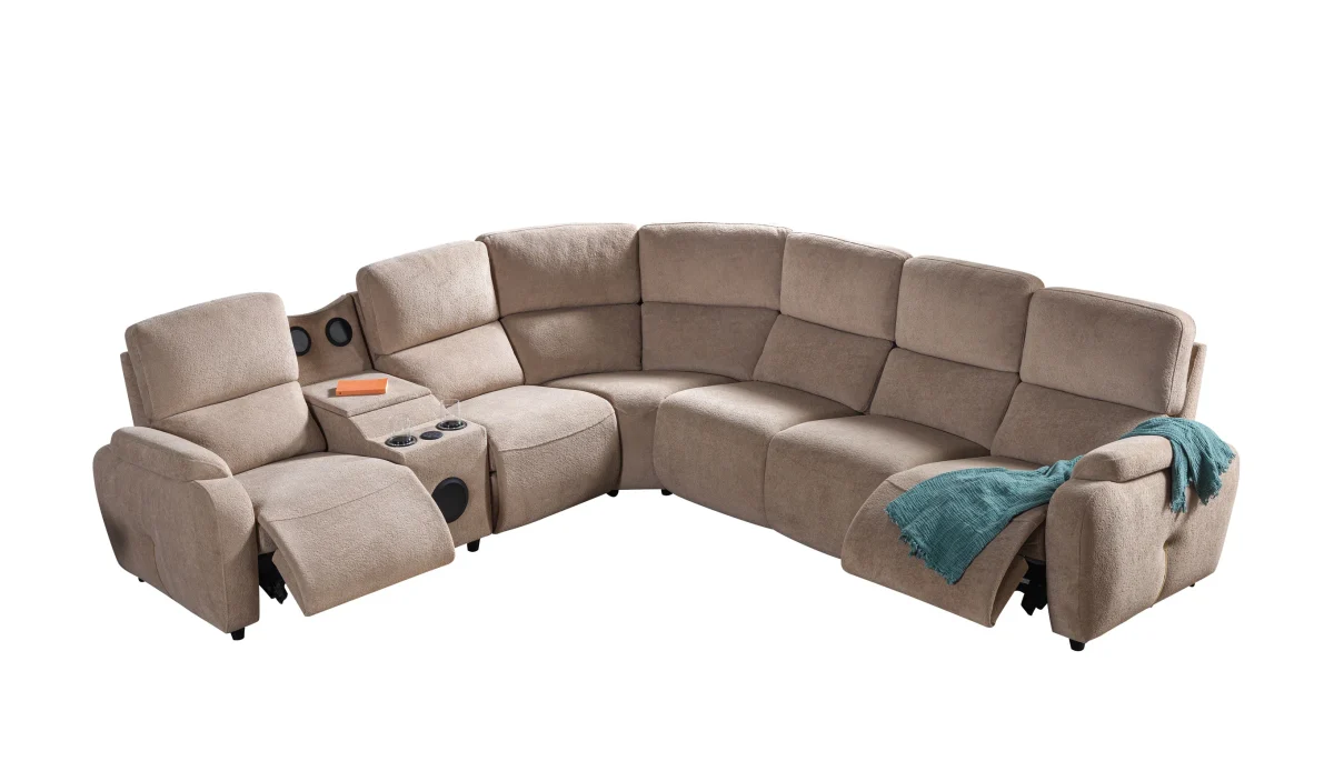 A detailed view of the Atlas Recliner Köşe Takımı, a contemporary L-shaped corner sectional sofa upholstered in textured beige fabric. The image shows its modern design with sleek lines and wide seats. The central console unit is featured, with an open lid, integrated cup holders, and a built-in Bluetooth speaker system visible on the side. The sofa is placed in a premium living room with light wood floors and textured wall paneling with LED backlighting.