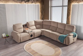 A detailed view of the Atlas Recliner Köşe Takımı, a contemporary L-shaped corner sectional sofa upholstered in textured beige fabric. The image shows its modern design with sleek lines and wide seats. The central console unit is featured, with an open lid, integrated cup holders, and a built-in Bluetooth speaker system visible on the side. The sofa is placed in a premium living room with light wood floors and textured wall paneling with LED backlighting.