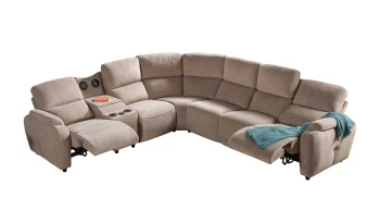 A detailed view of the Atlas Recliner Köşe Takımı, a contemporary L-shaped corner sectional sofa upholstered in textured beige fabric. The image shows its modern design with sleek lines and wide seats. The central console unit is featured, with an open lid, integrated cup holders, and a built-in Bluetooth speaker system visible on the side. The sofa is placed in a premium living room with light wood floors and textured wall paneling with LED backlighting.