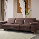 A detailed view of the Serena Motorized Triple Recliner, a premium brown three-seater sofa manufactured by Chairium, featuring extended motorized footrests and adjustable headrests on the outer seats.