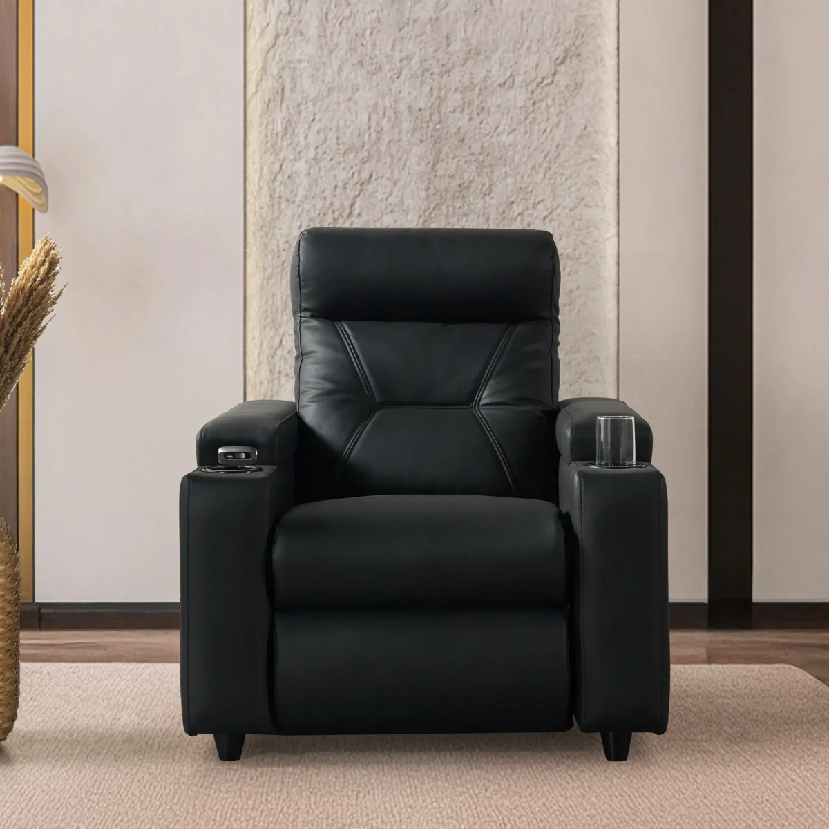 A front-facing view of the ZERO PLUS recliner, a luxurious black leather recliner chair with ergonomic stitched paneling and built-in cup holders. The recliner is centered on a light rug in a modern living room setting featuring elegant wood wall panels, accompanied by a tall woven vase holding decorative dry grass.