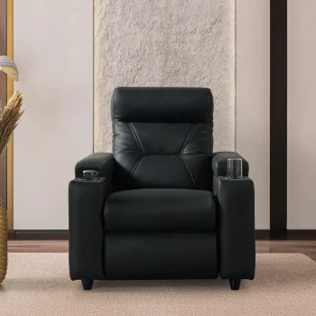 A front-facing view of the ZERO PLUS recliner, a luxurious black leather recliner chair with ergonomic stitched paneling and built-in cup holders. The recliner is centered on a light rug in a modern living room setting featuring elegant wood wall panels, accompanied by a tall woven vase holding decorative dry grass.