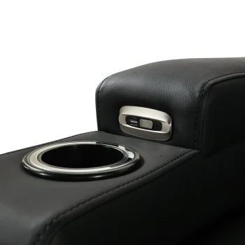 A front-facing view of the ZERO PLUS recliner, a luxurious black leather recliner chair with ergonomic stitched paneling and built-in cup holders. The recliner is centered on a light rug in a modern living room setting featuring elegant wood wall panels, accompanied by a tall woven vase holding decorative dry grass.